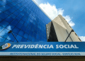 Foto da fachada do prédio sede da Previdência Social com logo e céu azul refletido no vidro.
