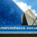 Foto da fachada do prédio sede da Previdência Social com logo e céu azul refletido no vidro.