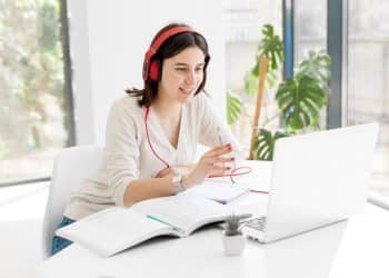 Jovem sorridente com fones de ouvido vermelhos estudando em um notebook, simbolizando o aprendizado de competências digitais e a educação online.
