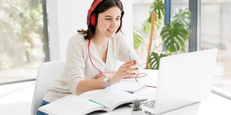 Jovem sorridente com fones de ouvido vermelhos estudando em um notebook, simbolizando o aprendizado de competências digitais e a educação online.