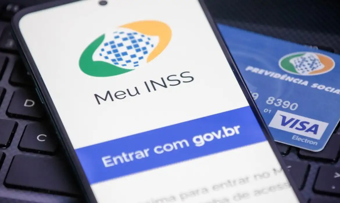 Tela de celular com app Meu INSS e cartão da Previdência Social Visa sobre teclado
