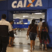Pessoas entrando na agência Caixa Econômica Federal com portas de vidro e fachada azul com logo da Caixa.