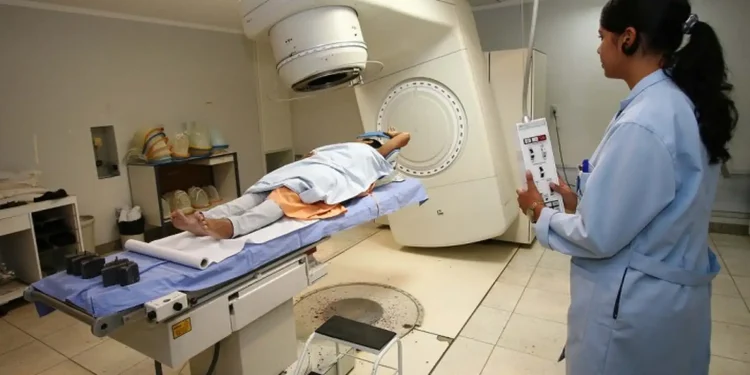 Mulher recebendo radioterapia em hospital com profissional de saúde operando aparelho