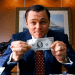 Leonardo DiCaprio vestido com terno segurando uma nota de dólar, cena icônica do filme O Lobo de Wall Street