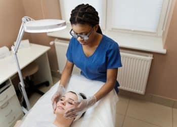 Esteticista aplica tratamento facial em cliente, ilustrando curso técnico de Estética.