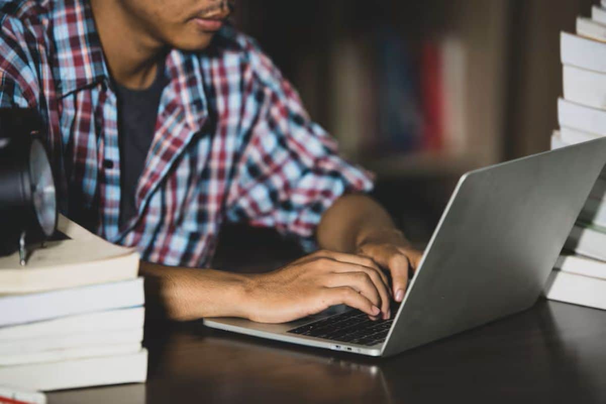 Pessoa realizando inscrição online para concurso da Câmara Municipal em um laptop, com livros ao redor.
