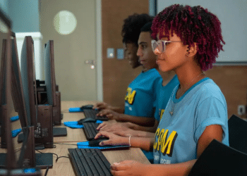 Grupo de jovens usando computadores em arquivo, com fones, concentrados no aprendizado de informática