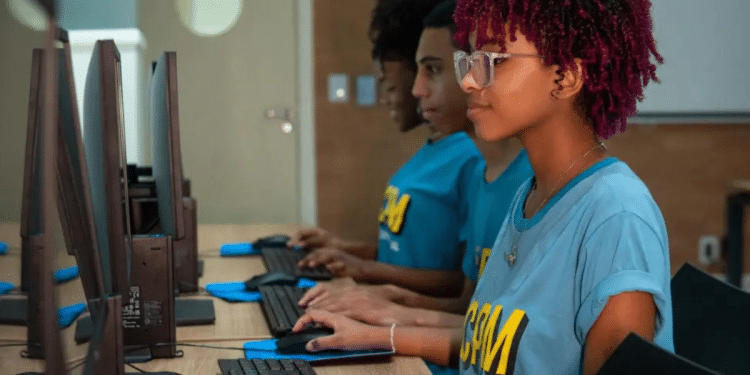 Grupo de jovens usando computadores em arquivo, com fones, concentrados no aprendizado de informática