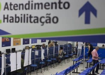 Atendimento no Departamento de Trânsito, com profissionais atendendo em balcões e pessoas aguardando em cadeiras.