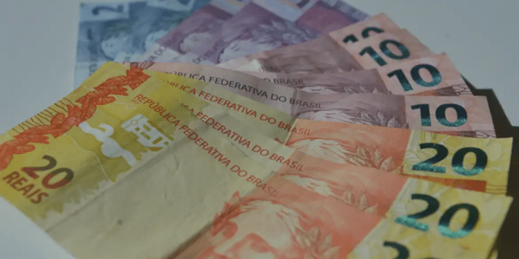 Cédulas de dinheiro em reais brasileiros com notas de 5, 10 e 20 reais espalhadas sobre superfície clara.