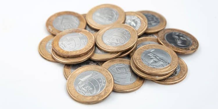 Pilha de moedas de R$ 1 do Plano Real, alertando sobre a moeda de 2016 com o erro do reverso invertido.