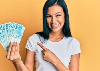 Imagem ilustrativa de uma pessoa sorrindo e segurando várias cédulas de R$100, simbolizando o aumento do salário em profissões que não exigem diploma universitário.