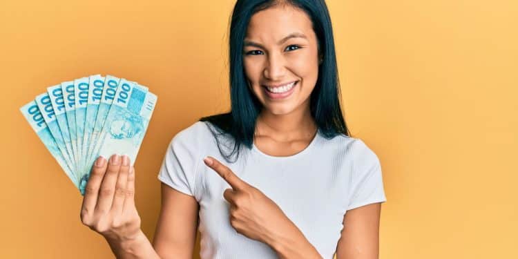 Imagem ilustrativa de uma pessoa sorrindo e segurando várias cédulas de R$100, simbolizando o aumento do salário em profissões que não exigem diploma universitário.