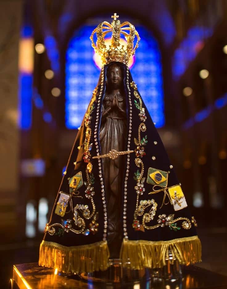 Imagem de Nossa Senhora Aparecida, a Padroeira do Brasil, com manto azul escuro e coroa dourada, representando a fé católica e o milagre de 1717.