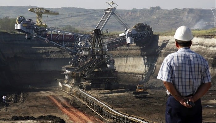 Imagem de uma máquina de mineração em operação, vista de um trabalhador observando o processo, simbolizando as oportunidades lucrativas nas áreas de energia e mineração.