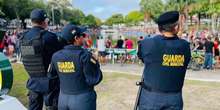 Três guardas civis municipais uniformizados patrulhando área pública com pessoas ao fundo