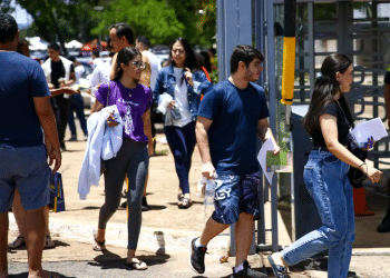 Grupo de jovens caminhando para fora do local de prova com documentos nas mãos em dia de vestibular