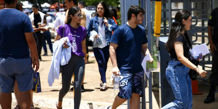 Grupo de jovens caminhando para fora do local de prova com documentos nas mãos em dia de vestibular