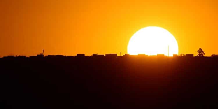 Um pôr do sol alaranjado sobre a silhueta de uma cidade, simbolizando as mudanças de horário do verão.