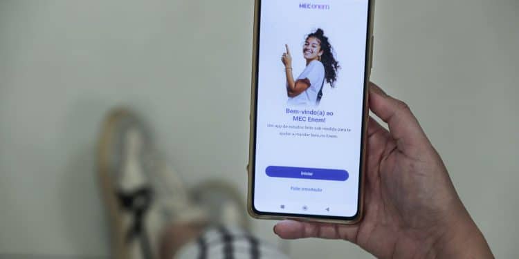 Pessoa segura um celular exibindo a tela inicial do aplicativo MEC Enem.