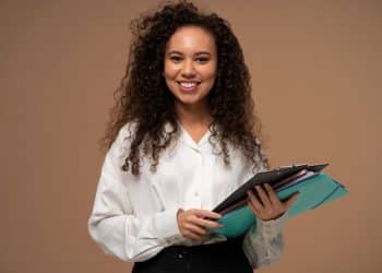 Mulher jovem e sorridente segurando pastas e documentos, representando o sucesso e o planejamento de carreira para as profissões do futuro no Brasil.
