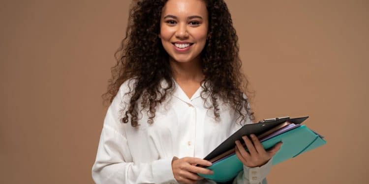 Mulher jovem e sorridente segurando pastas e documentos, representando o sucesso e o planejamento de carreira para as profissões do futuro no Brasil.