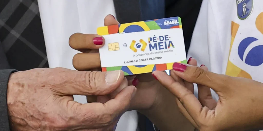 Cartão do programa Pé-de-Meia sendo entregue a estudante beneficiada