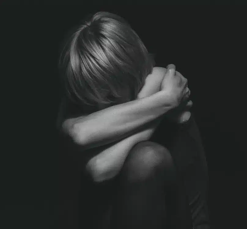Pessoa em um momento de introspecção, com os braços abraçando as pernas, mostrando vulnerabilidade e sentimentos profundos.
