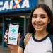 Jovem sorrindo segura celular com transferência via Pix de R$200 em frente a agência da Caixa.