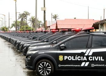 Várias viaturas pretas da Polícia Civil do Ceará alinhadas em fila sob chuva com sirenes vermelhas ligadas.