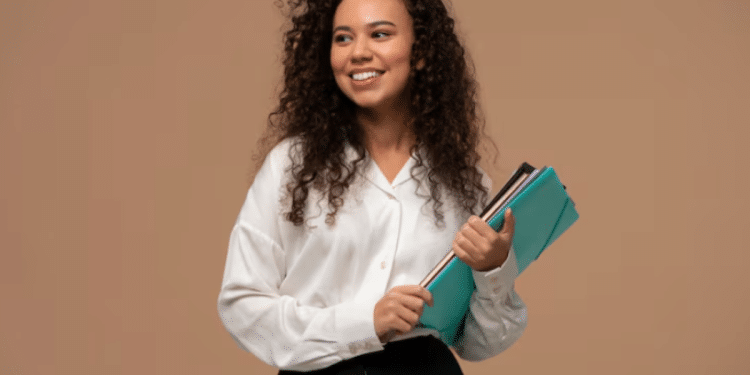 Mulher jovem com cabelo cacheado sorrindo e segurando várias pastas coloridas sobre fundo bege