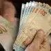 Mãos segurando notas de real representando o Saque Calamidade do FGTS liberado para trabalhadores afetados por desastres naturais