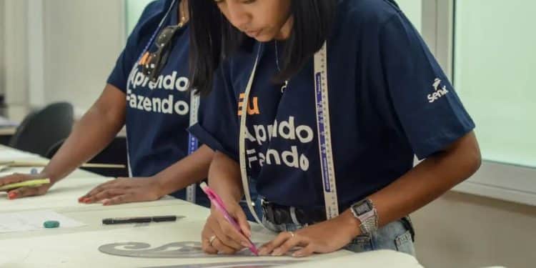 Duas alunas do Senac em uma aula prática, uma delas desenhando moldes em tecido, simbolizando o aprendizado técnico e profissionalizante.