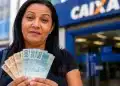 Mulher segura notas de real em frente a uma agência da Caixa, representando a solicitação do saque de R$ 6.220 do FGTS até 23 de julho.