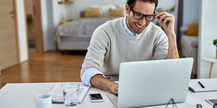 Homem-feliz-trabalhando-de-casa-em-home-office-com-notebook-para-artigo-sobre-profissões-que-pagam-em-dólar-2025