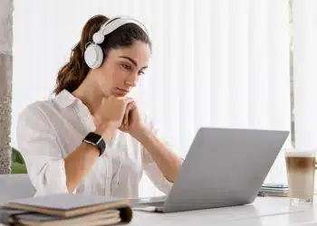 Mulher trabalhando em um laptop com fones de ouvido, representando a adaptação ao mundo digital por meio de cursos de formação.