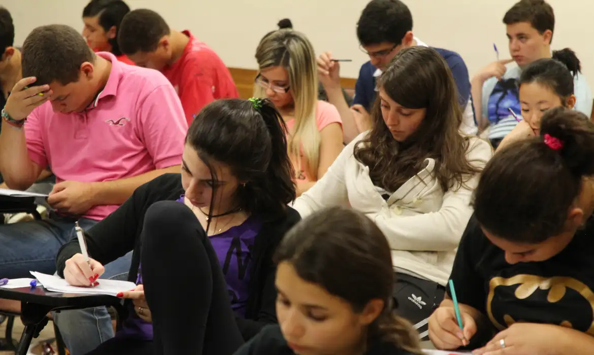 Alunos em sala de aula concentrados escrevendo em cadernos durante uma prova