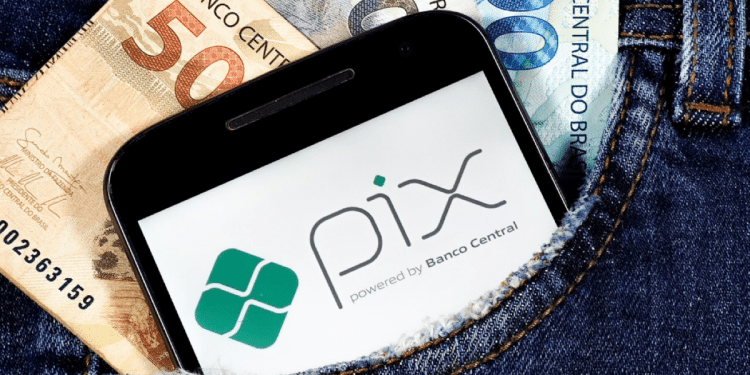 Cédulas de real e celular com logo do Pix dentro do bolso de uma calça jeans