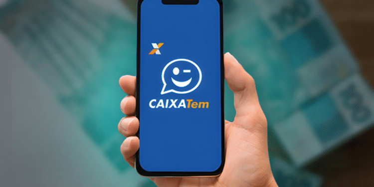 Mão segurando um smartphone com o aplicativo Caixa Tem aberto, mostrando o logotipo e um ícone de "piscadinha" sobre um fundo de notas de R$ 100 desfocadas, simbolizando o pagamento e a facilidade de acesso.