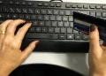 Mãos femininas digitando no teclado enquanto seguram um cartão de crédito azul para compras online.