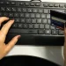 Mãos femininas digitando no teclado enquanto seguram um cartão de crédito azul para compras online.
