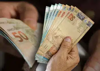 Pessoa segurando leque de cédulas de cinquenta reais representando pagamento de R$ 200 do Pé-de-Meia Enem