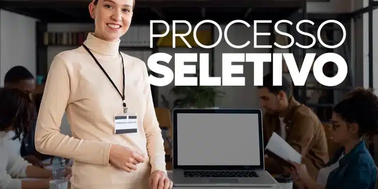 Mulher sorridente com crachá apresentando processo seletivo em escritório moderno e equipe ao fundo