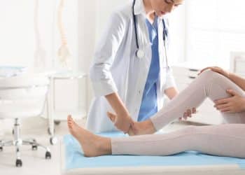 Médica ortopedista examinando a perna de um paciente em consultório. Representa profissões de alto salário e baixo estresse, como a ortopedia.