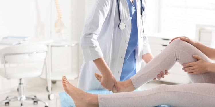 Médica ortopedista examinando a perna de um paciente em consultório. Representa profissões de alto salário e baixo estresse, como a ortopedia.