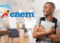 Jovem sorridente de camiseta cinza, carregando notebook, ao lado do logo do Enem em ambiente de sala de estudos.