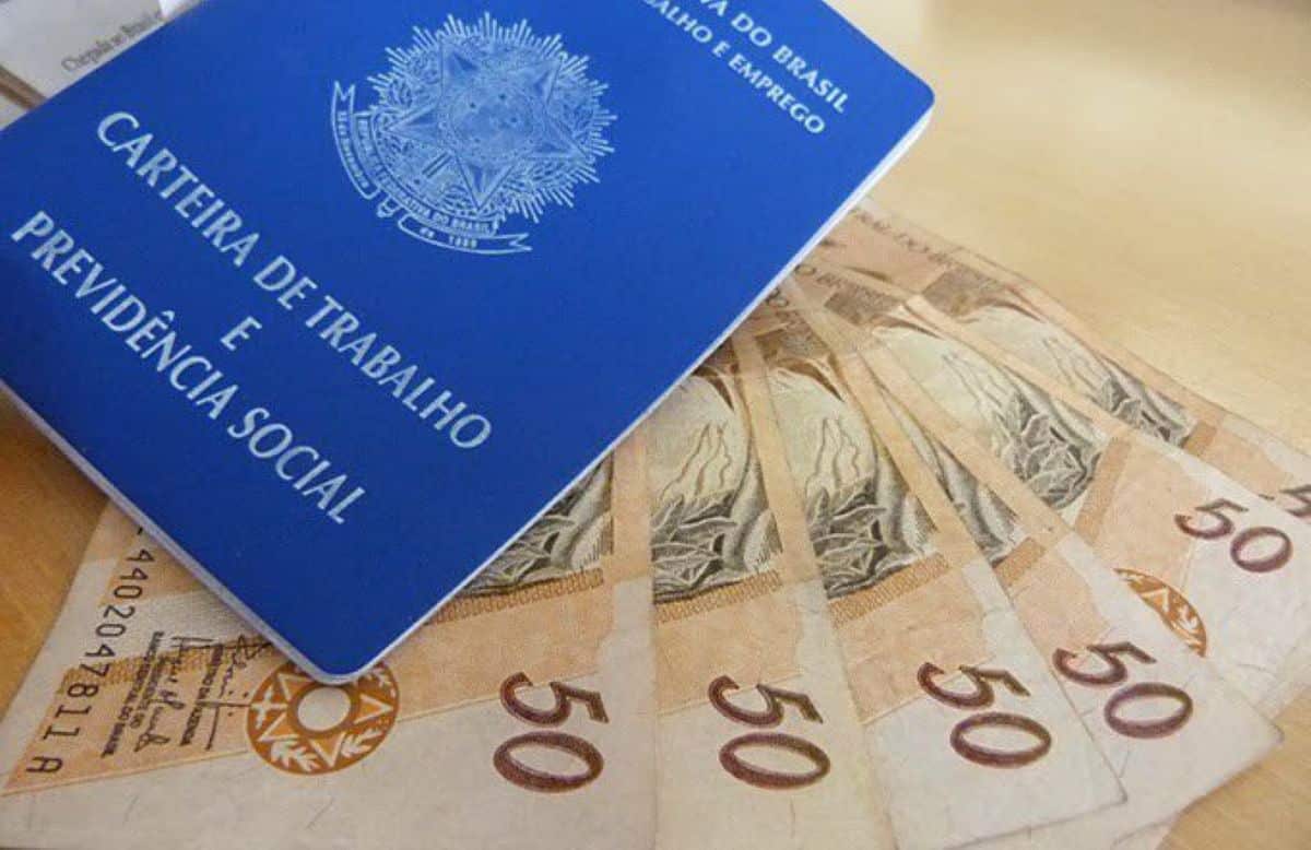 Carteira de Trabalho e Previdência Social aberta sobre notas de 50 reais, representando o cálculo e o direito ao 13º salário.