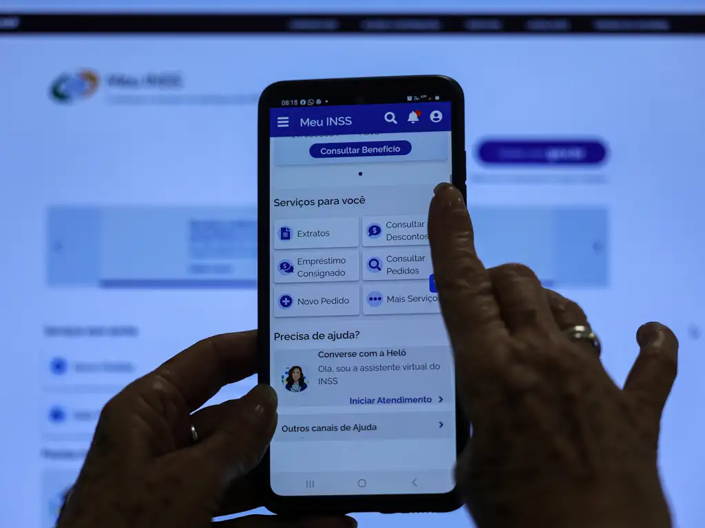 Meu INSS. Usuário utilizando o Aplicativo Meu INSS para navegar pelo menu de serviços digitais, incluindo "Extratos", "Consultar Pedidos" e "Empréstimo Consignado".