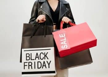 Mulher segurando sacolas de compras da Black Friday, incluindo uma com o rótulo 'SALE' e outra com 'BLACK FRIDAY', destacando o frenesi de compras de beleza e os riscos de fraude.