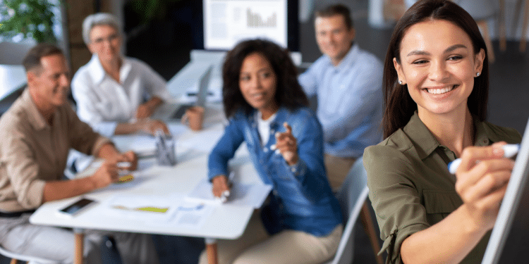 Grupo de profissionais em reunião com mulher escrevendo no quadro branco durante apresentação.